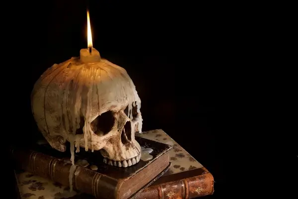 صورة تحتوي على جمجمة فوقها شمعة و كتب كيفية عمل السحر في المنزل